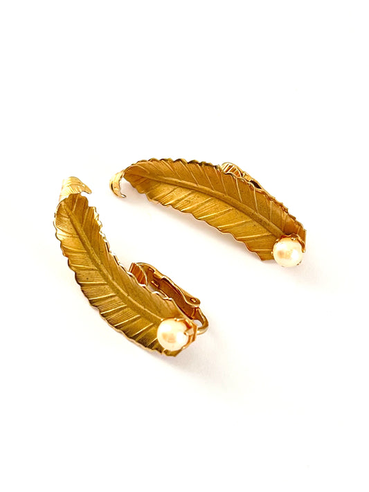 Gold feather-shaped earrings on a white background