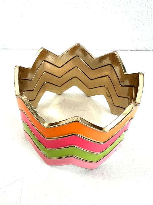 A chevron-style cuff bracelet with multiple stacked zigzag bands in gold, orange, pink, and light green, photographed on a plain white background.