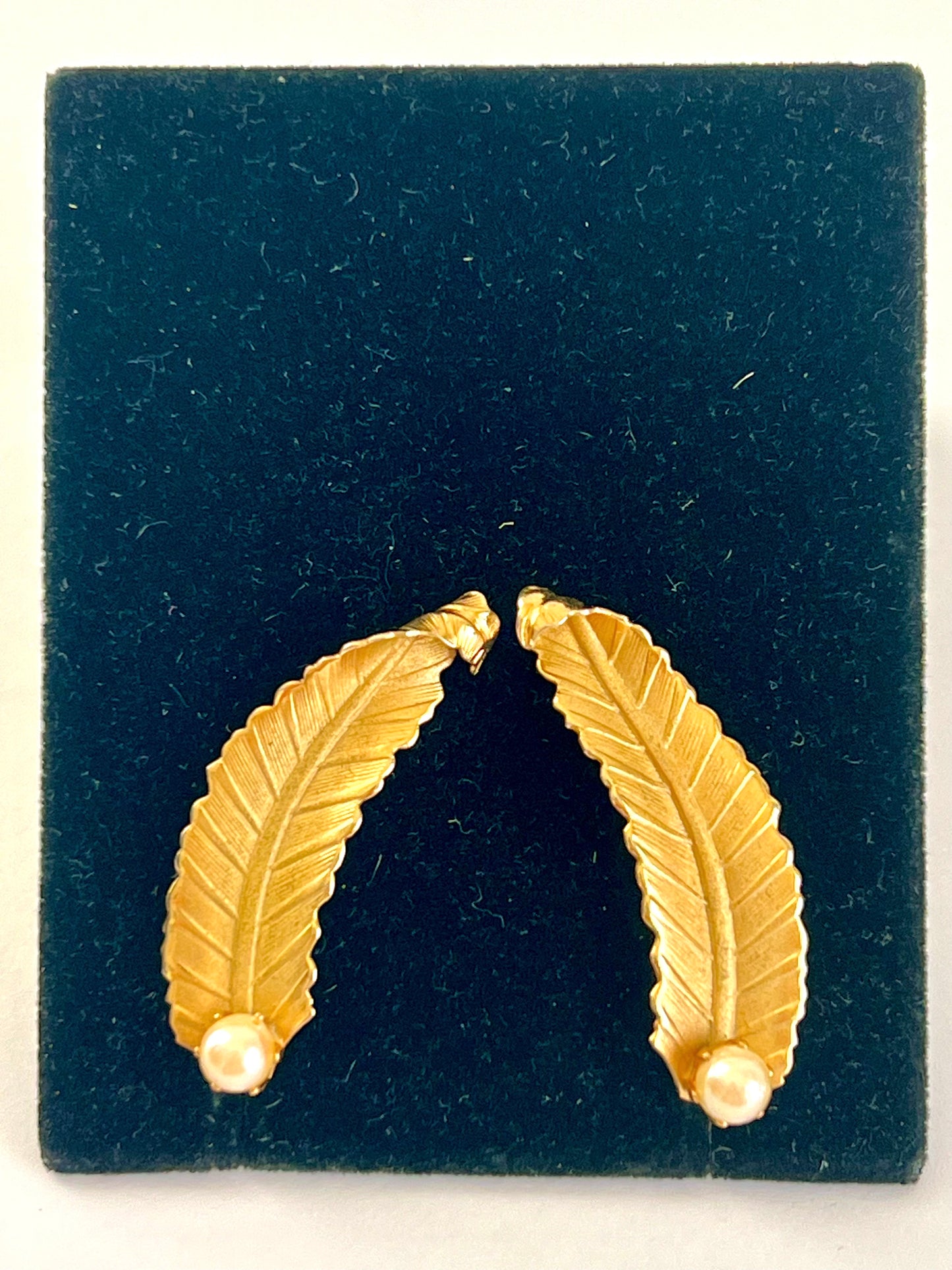 Pair of gold feather-shaped earrings on a dark blue display card.
