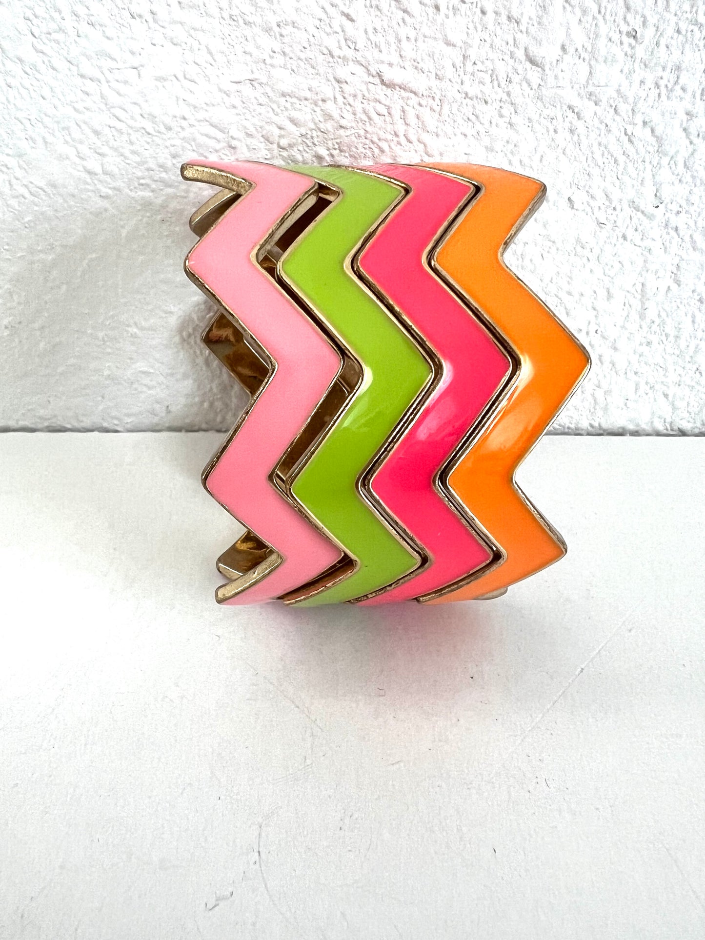 Four chevron cuff bracelets featuring alternating zigzag bands of pink, lime green, hot pink, and orange, outlined with gold-toned metal.