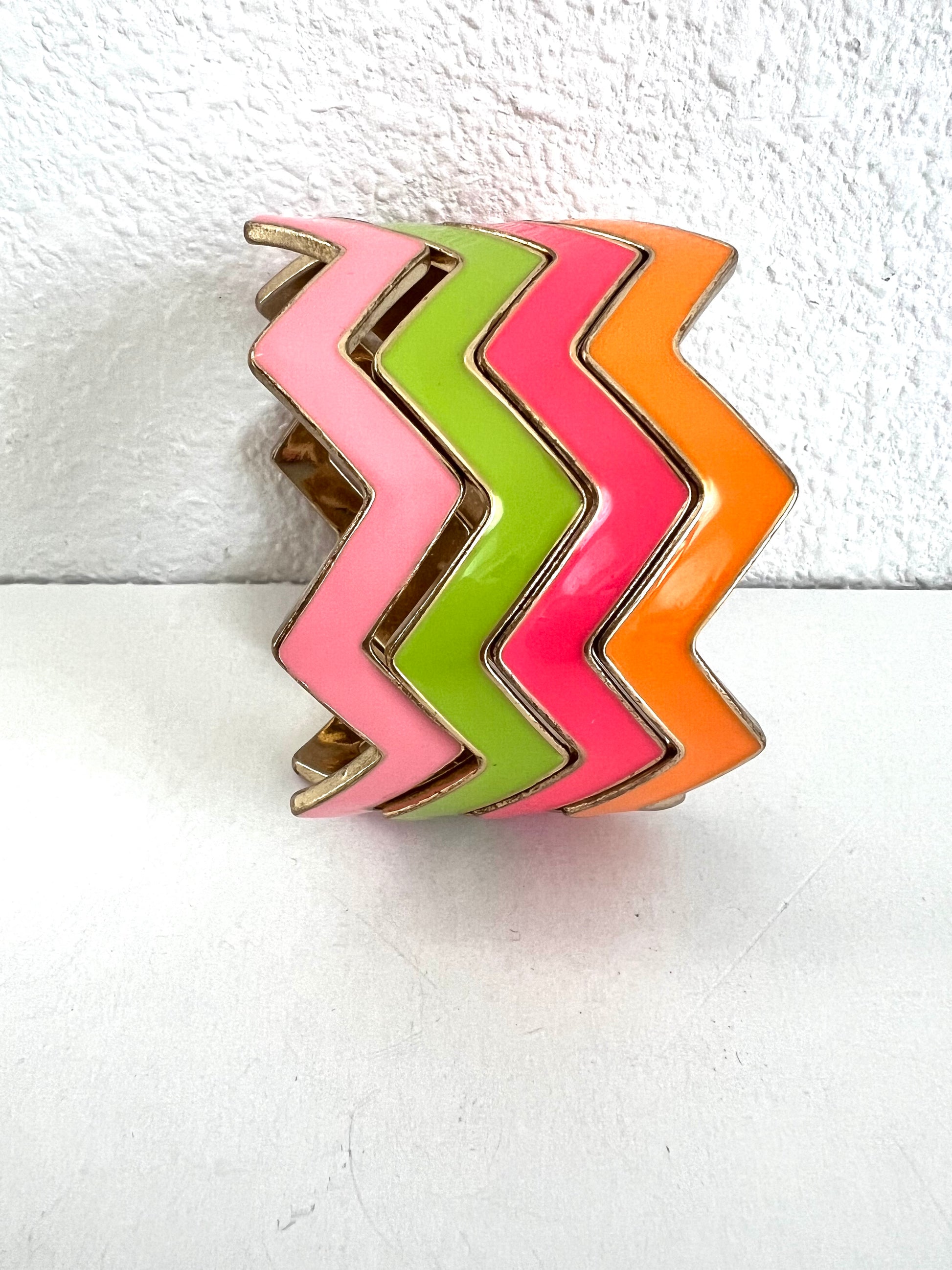 Four chevron cuff bracelets featuring alternating zigzag bands of pink, lime green, hot pink, and orange, outlined with gold-toned metal.