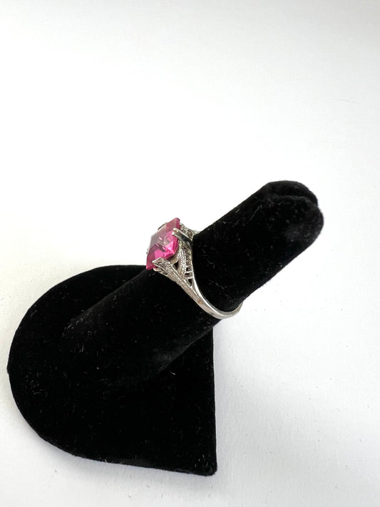 A silver ring with a pink gemstone displayed on a black velvet ring stand against a white background.