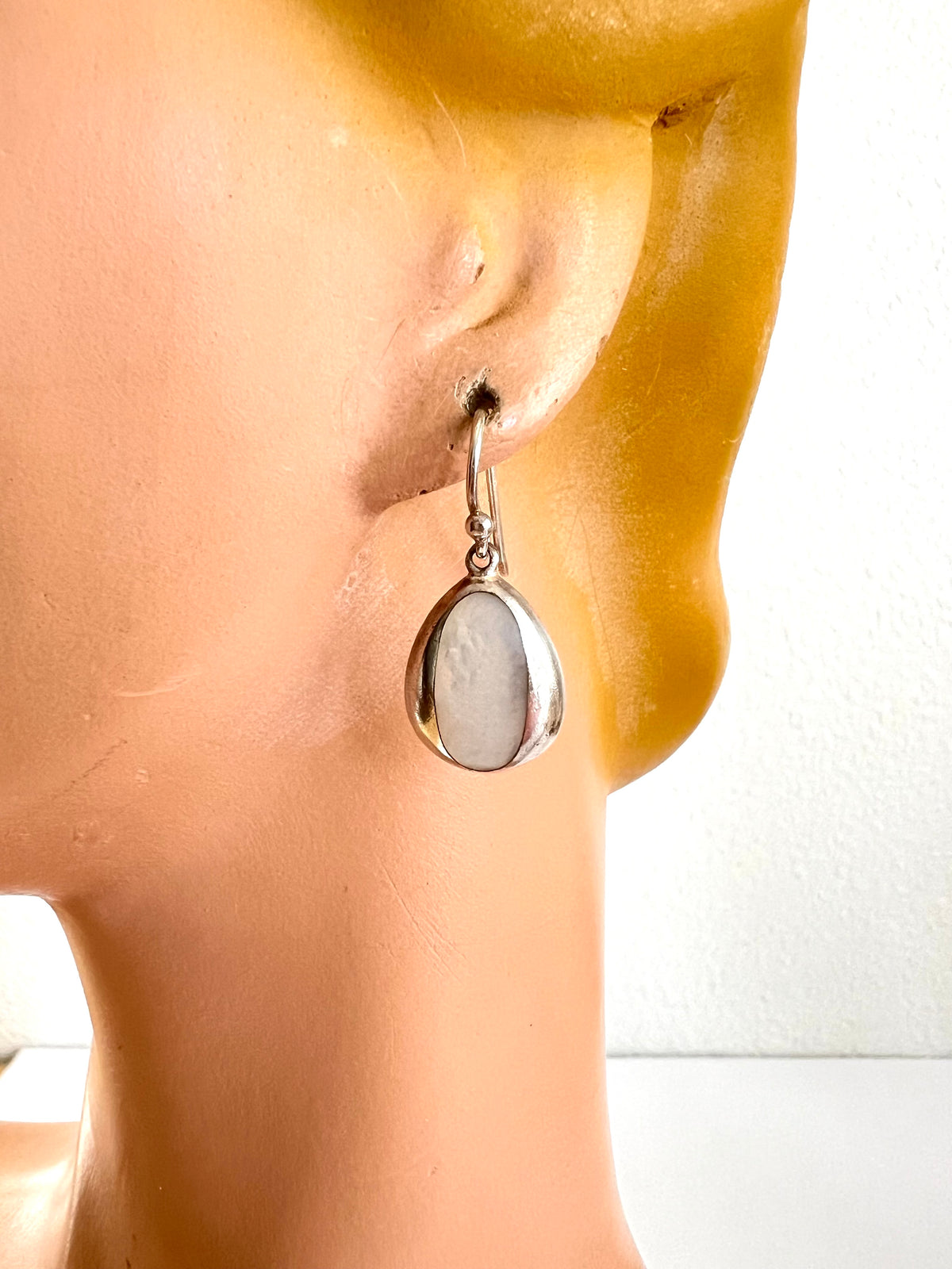 A close-up of a silver drop earring with a teardrop-shaped white stone, displayed on a mannequin head against a plain white background.