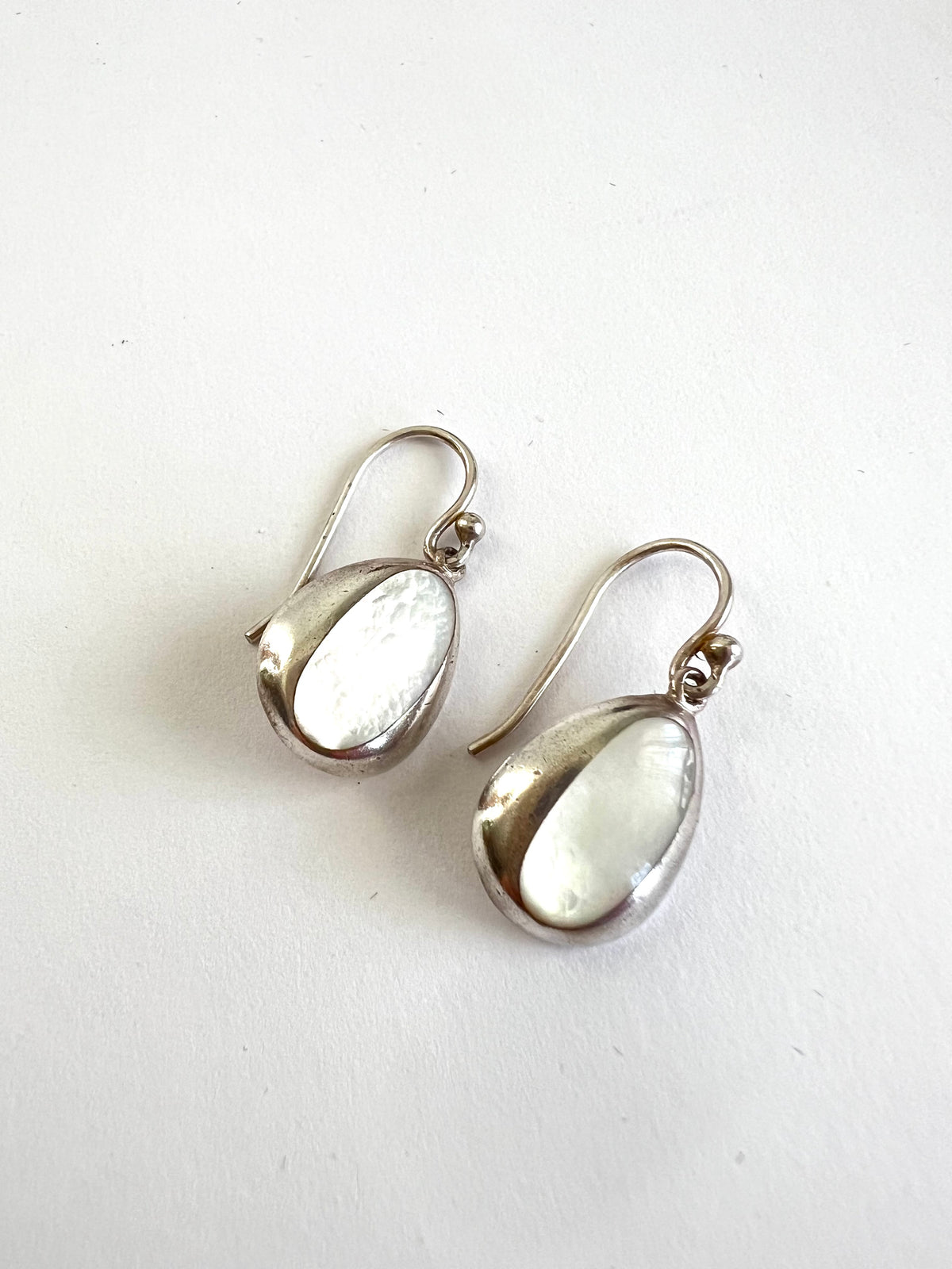 A pair of silver teardrop dangle earrings with Mother of Pearl centers, displayed on a plain white surface.