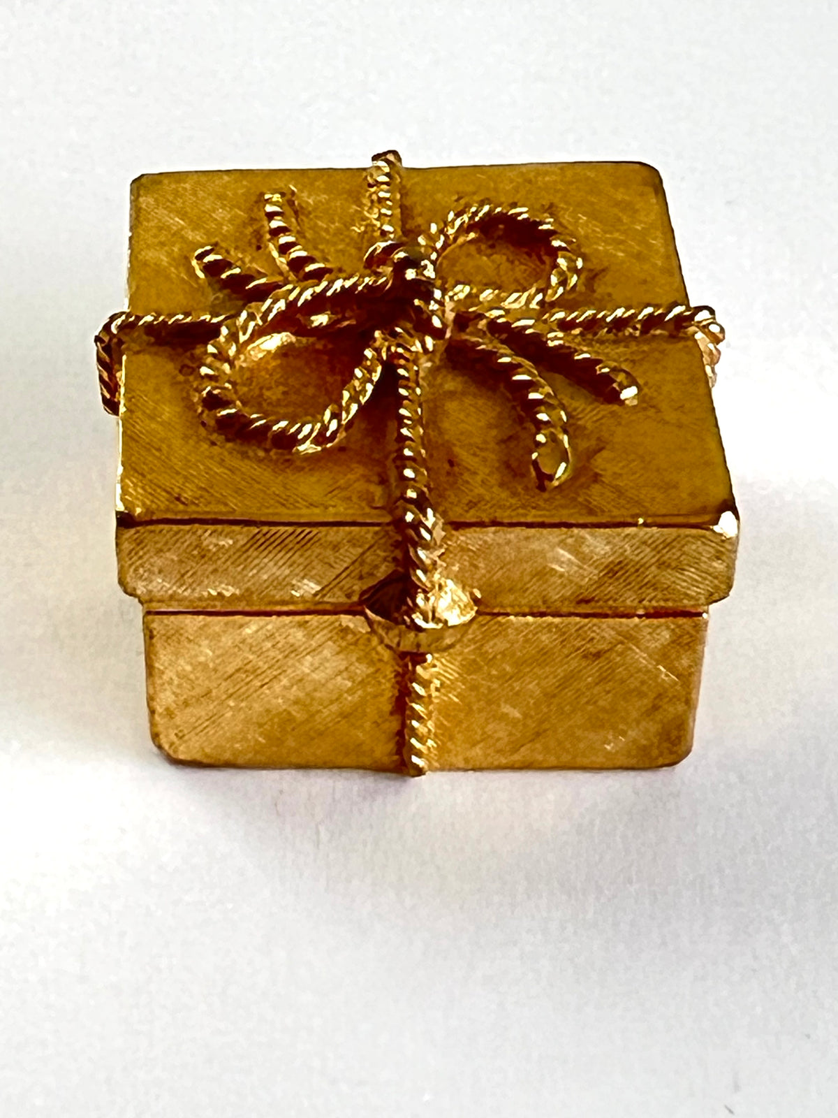 A small gold gift box with a textured finish, wrapped in gold rope-style ribbon and bow, set against a plain white background.