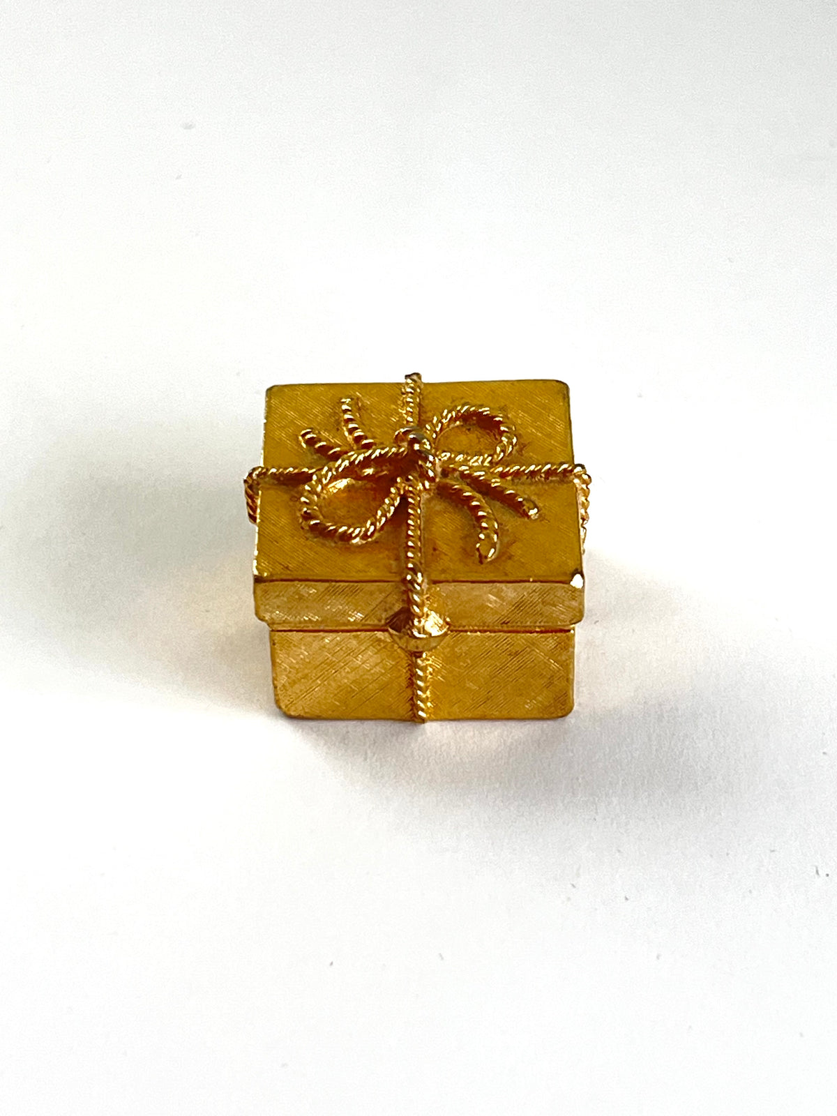 A small gold gift box charm with a textured finish, wrapped in gold ribbon with a bow, set against a plain white background.